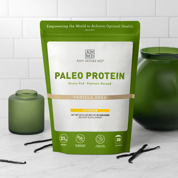 Resealable bag of AMMD Vanilla Bean flavored Paleo Protein sitting on a wooden countertop, with white tile background.