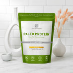 Resealable bag of AMMD Unflavored Paleo Protein sitting on a wooden countertop, with white tile background.