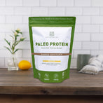 Resealable bag of AMMD Double Chocolate flavored Paleo Protein sitting on a wooden countertop, with white tile background.