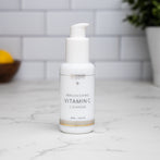 A travel size bottle of Vitamin C Cleanser sitting on a granite bathroom countertop