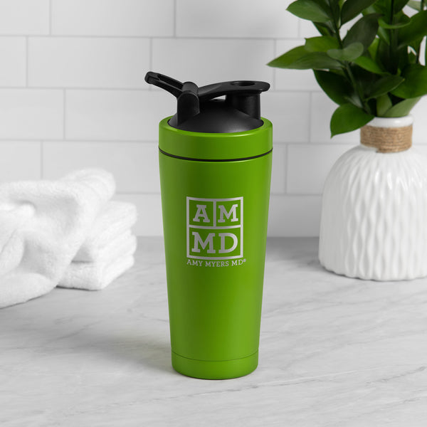 A green and silver Amy Myers MD branded shaker bottle is shown sitting on a light gray kitchen counter with a white tile backsplash.